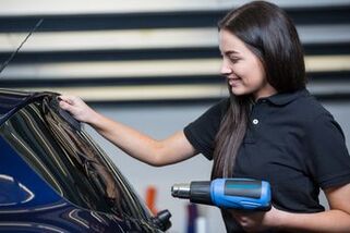 Picture of dark haired girl installing window tint with blue heat gun