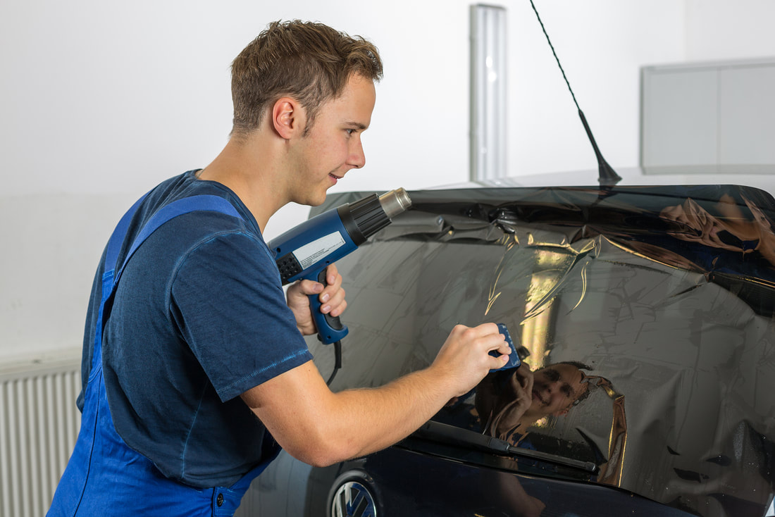 Picture of man installing window tinting on a car with a blue heat gun